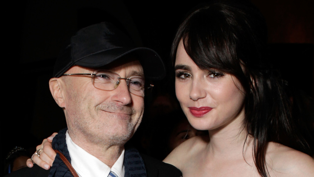 Phil Collins, Lily Collins smiling while posing arm in arm