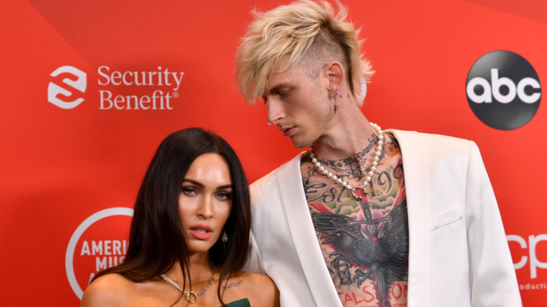 Megan Fox posing for cameras next to Machine Gun Kelly as he looks down at her