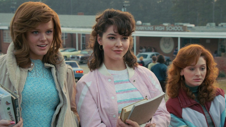 Madelyn Cline as Tina smiling while standing between two friends