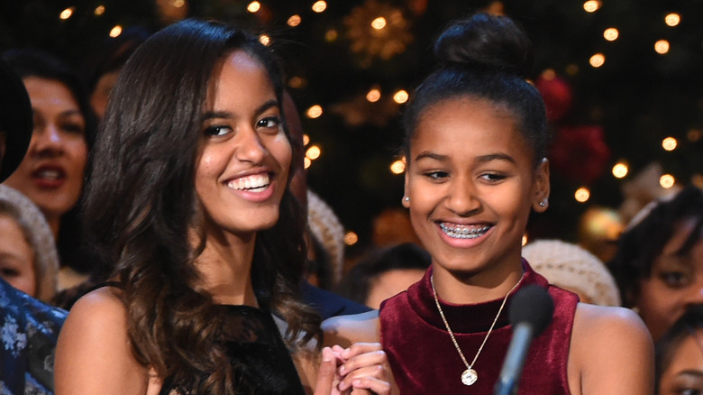 Malia Obama wearing a black strapless dress with Sasha Obama wearing a high neck red velvet dress