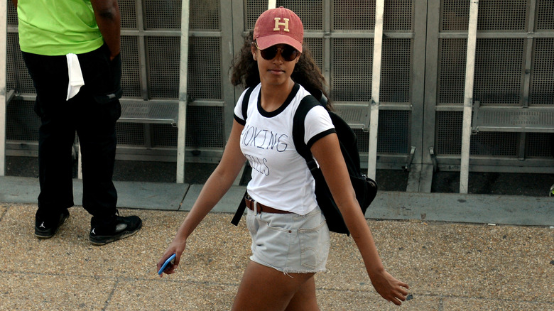 Malia Obama wearing a white t-shirt, denim shorts, and crimson ball cap