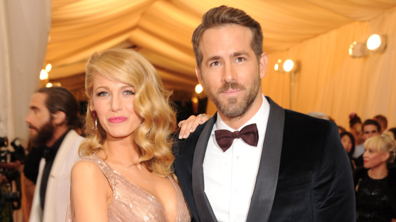 Blake Lively wearing a silver strappy gown and Ryan Reynolds wearing a black tuxedo and maroon bowtie at formal event