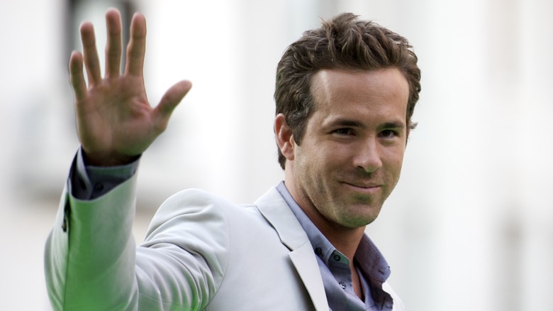 Ryan Reynolds wearing a light grey jacket while waving