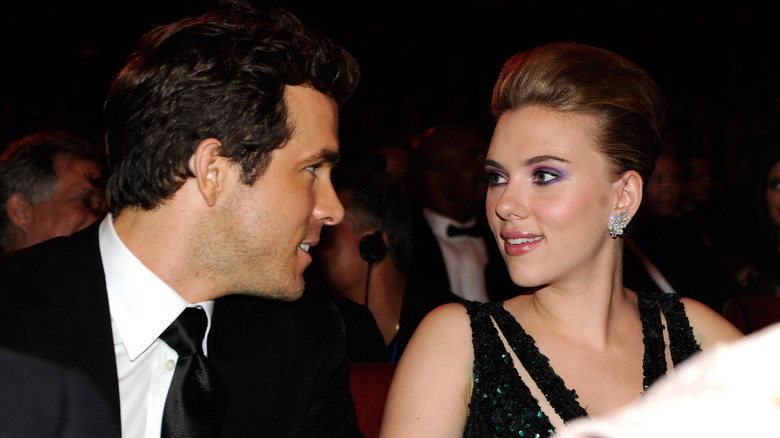 Ryan Reynolds wearing a tuxedo and Scarlett Johansson wearing a black strappy gown while seated