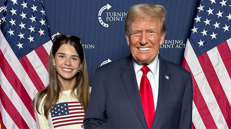 Kai Trump posing with Donald Trump by American flags