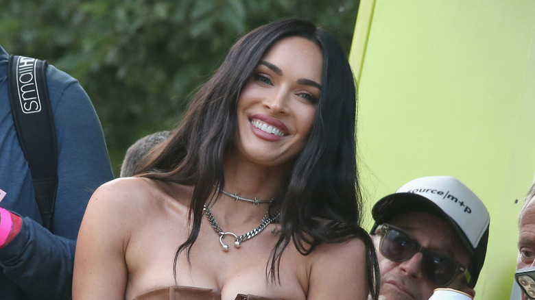 Megan Fox smiling and wearing pink lipstick and a silver barbed wire choker