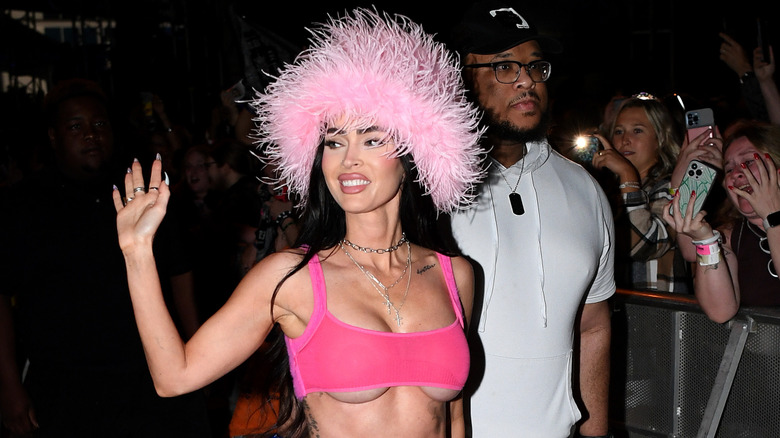 Megan Fox wearing a pink feather hat and waving