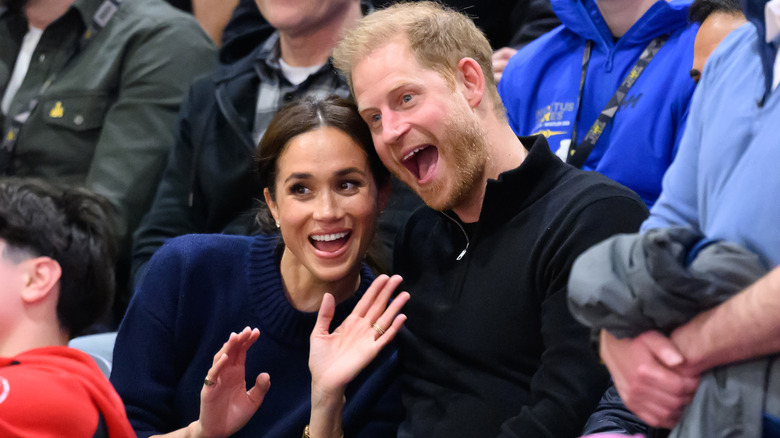 Prince Harry and Meghan Markle smiling while sitting in crowd