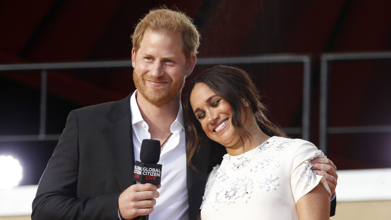 Prince Harry, Duke of Sussex puts arm around Meghan, Duchess of Sussex on stage