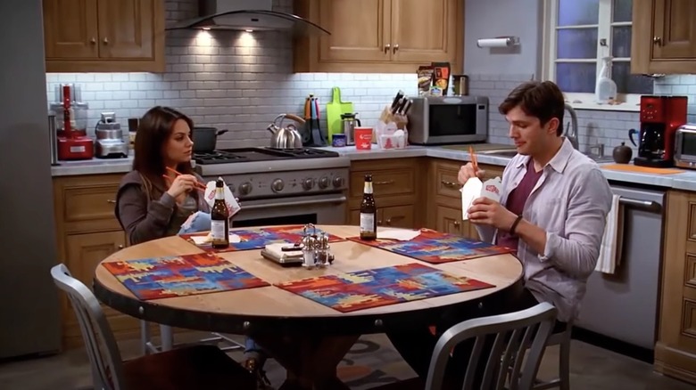 Mila Kunis and Ashton Kutcher sitting at a table on Two and a Half Men
