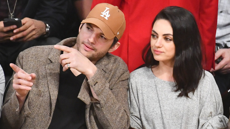 Ashton Kutcher pointing at something beside Mila Kunis