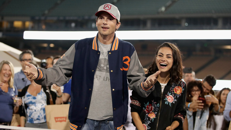 Ashton Kutcher with his arms in the air, Mila Kunis laughing