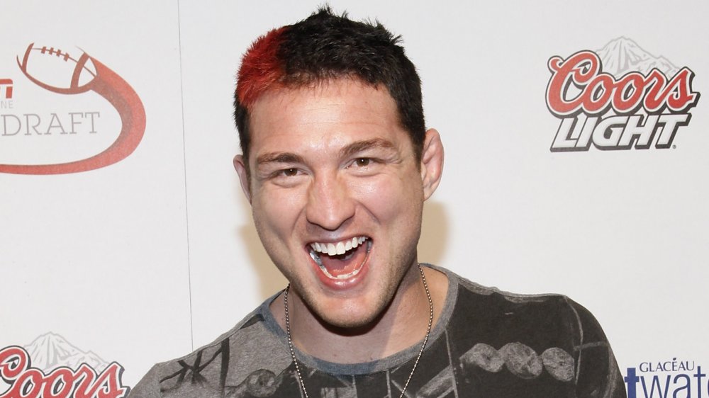 Jason Miller in a printed t-shirt and a red streak in his hair, smiling big at an event