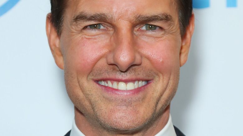 Tom Cruise smiles in a dark suit and tie.