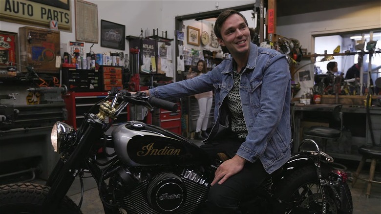 Nicholas Hoult sitting on an Indian motorcycle, smiling