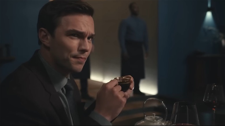 Nicholas Hoult drinking from small cup and looking perplexed