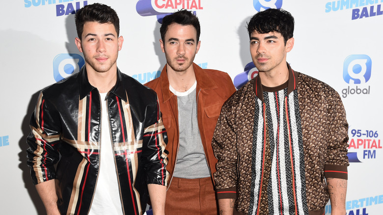 Nick Jonas poses for the camera while brothers Kevin and Joe look off camera on the red carpet