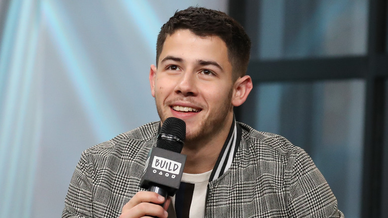 Nick Jonas smiling and holding a microphone