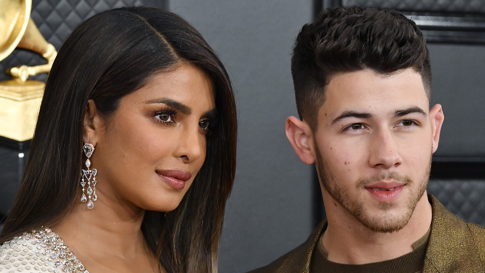 Priyanka Chopra and Nick Jonas pose for cameras together, facing opposite directions 