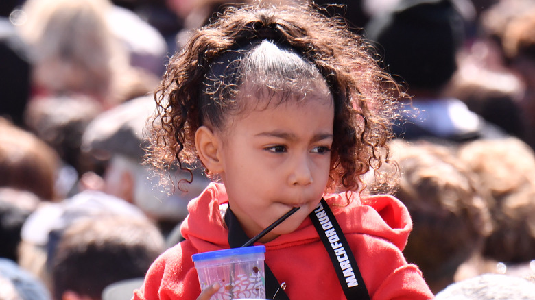 North West looking sideways while sipping from a cup