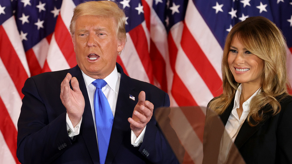 Donald Trump clapping next to smiling Melania Trump