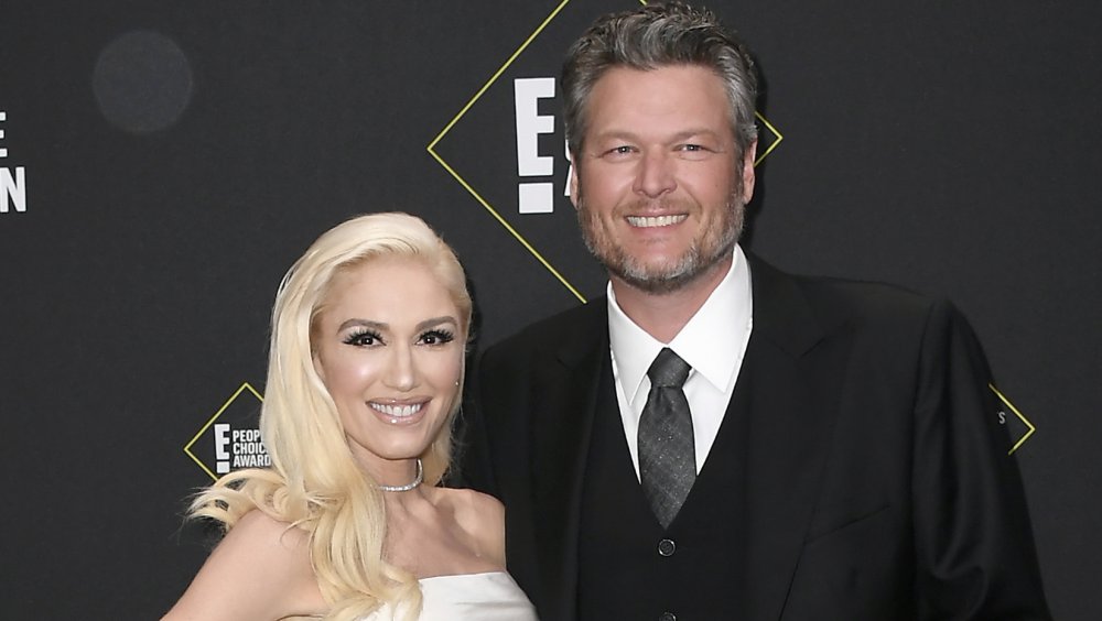 Gwen Stefani in a white dress, Blake Shelton in a three-piece black suit, smiling on the People's Choice Awards red carpet