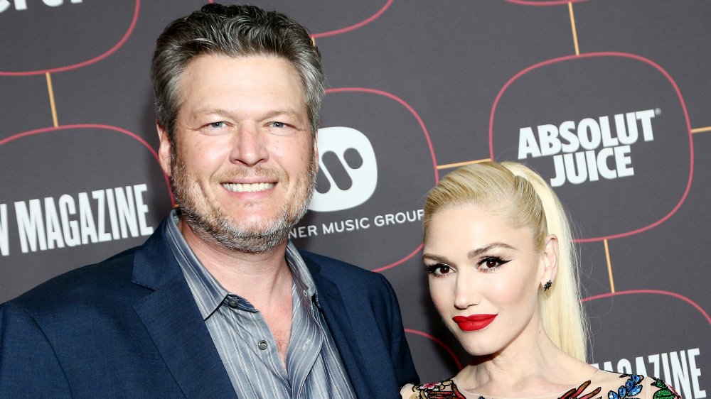 Blake Shelton in a blue blazer and striped shirt, Gwen Stefani in a floral-printed top, posing together at an event