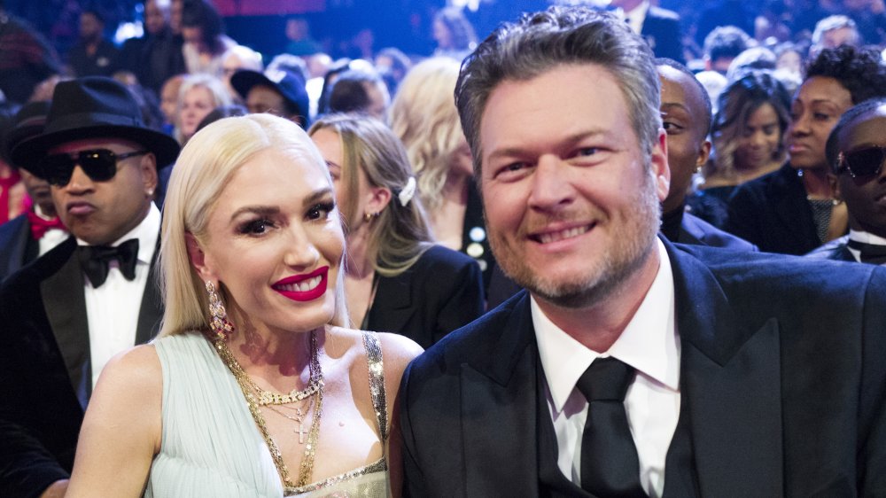 Gwen Stefani in a light teal dress, Blake Shelton in a black three-piece suit, both smiling while sitting at an awards show