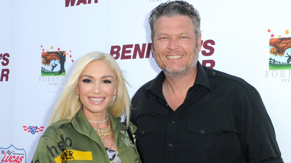 Gwen Stefani in a green jacket, Blake Shelton in a black button-up shirt, both smiling