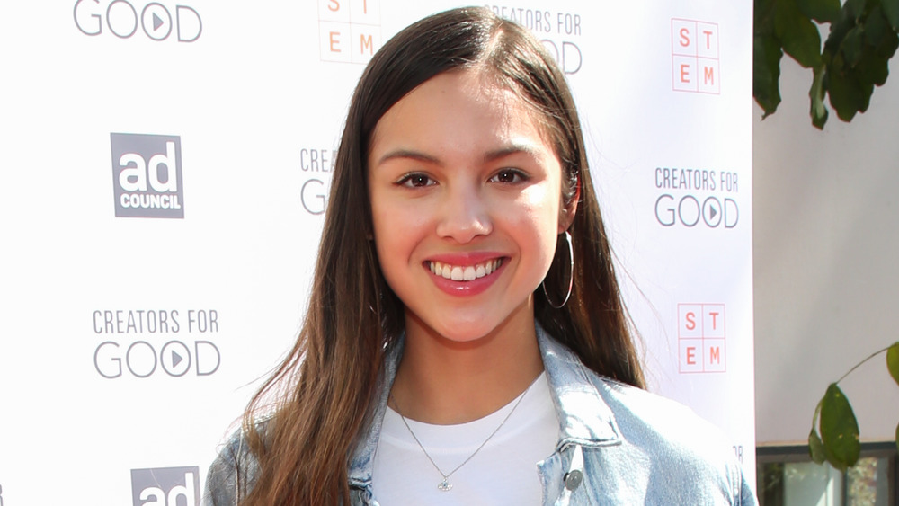 Olivia Rodrigo, smiling, hair down, jean jacket, on red carpet 