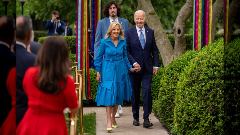 Jill Biden wearing a blue shirt dress and holding hands with Joe Biden