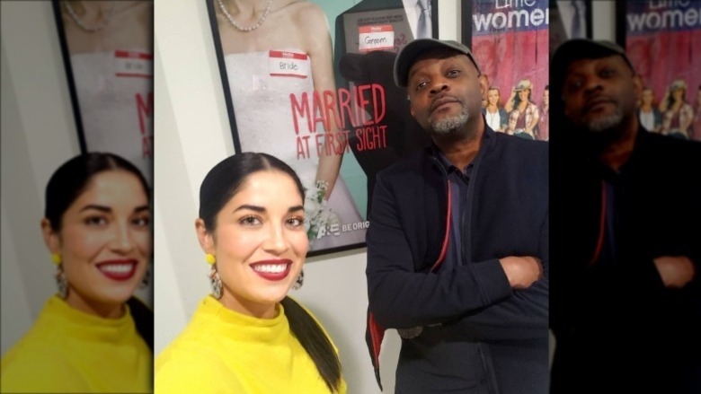 Dr. Viviana Coles and Pastor Calvin Roberson posing in front of a Married At First Sight poster