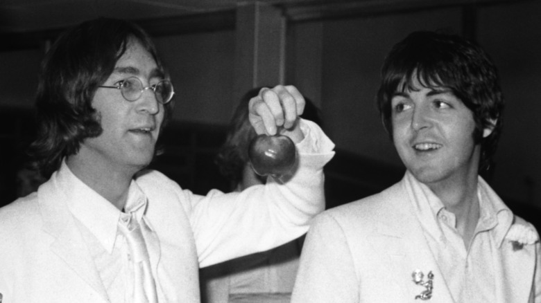 John Lennon holding an apple as Paul McCartney smiles