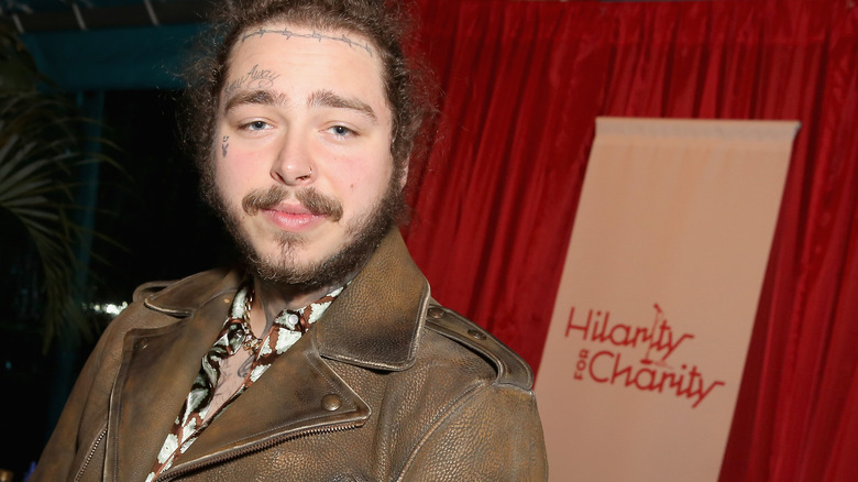 Post Malone smiling in front of a "Hilarity for Charity" sign