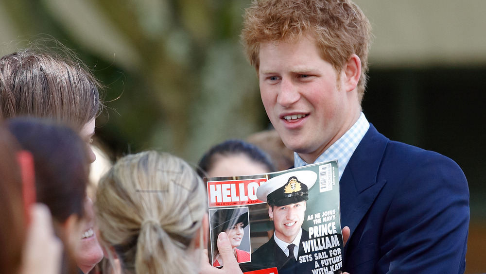 Prince Harry holding up picture of Prince William on a tabloid