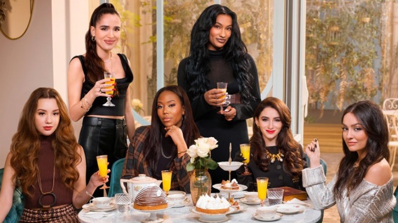 The cast of "Girlfriends in Paris" posing around table drinking mimosas