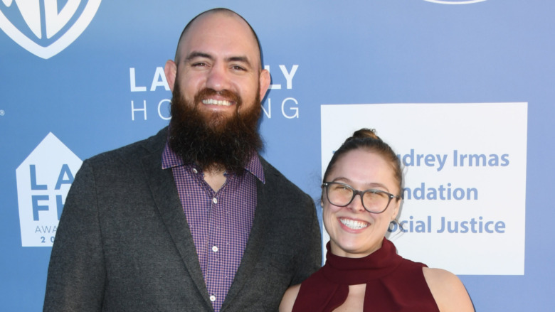 Travis Browne and Ronda Rousey, wearing glasses, smiling and posing for cameras