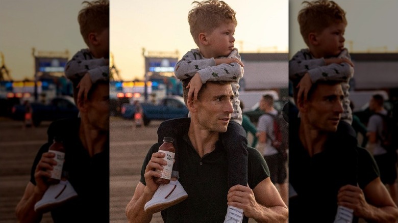 Andrew Walker holds Little West juice bottle while carrying his son on his shoulders