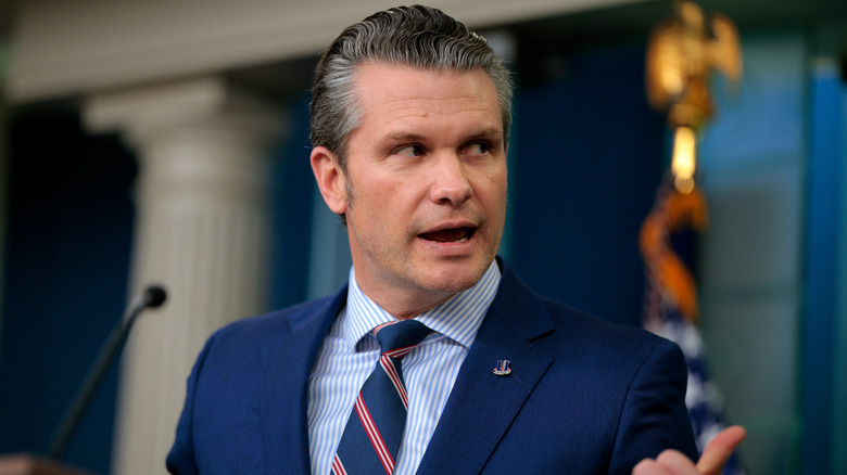 Pete Hegseth gestures behind him while addressing reporters.