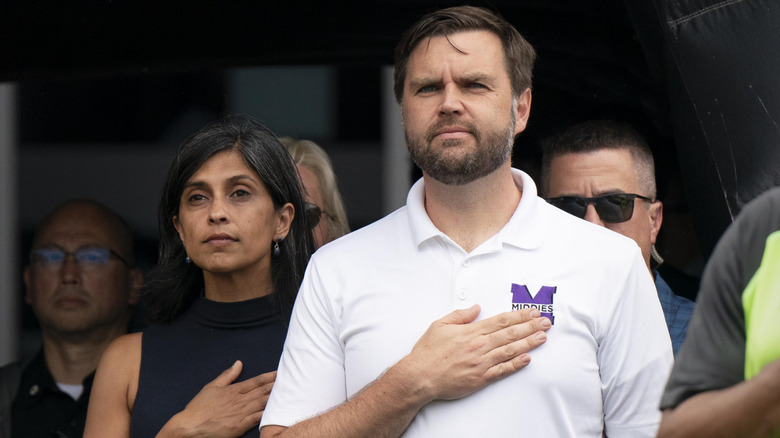 Usha and JD Vance standing side-by-side with their hands over their hearts.