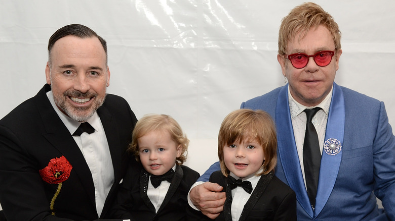 Elton John seated and posing with his husband and sons