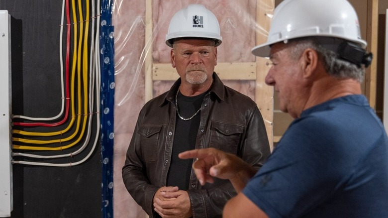 Mike Holmes wearing hard hat whie speaking to another man at a construction site