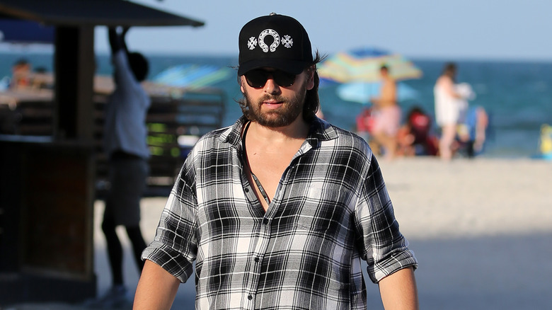 Scott Disick walking on beach in cap and dark sunglasses