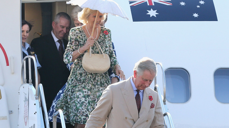 Queen Camilla and King Charles walking down the stairs of a plane