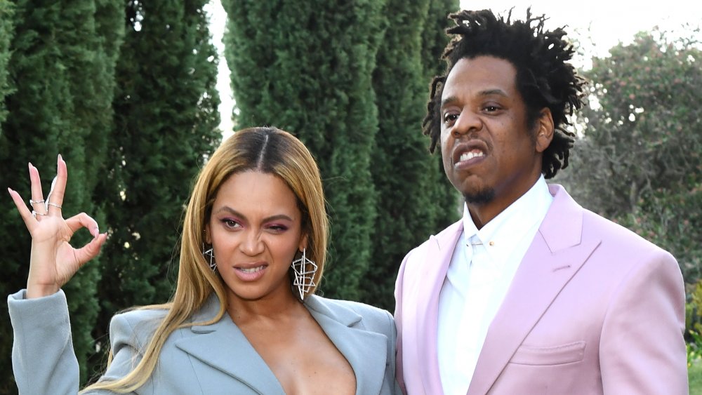 Beyoncé in a blue suit-dress, and Jay-Z in a pink suit, posing outside together