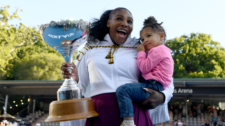 Serena Williams holds trophy and daughter