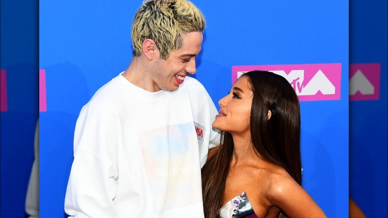 Pete Davidson looking down at Ariana Grande, both smiling