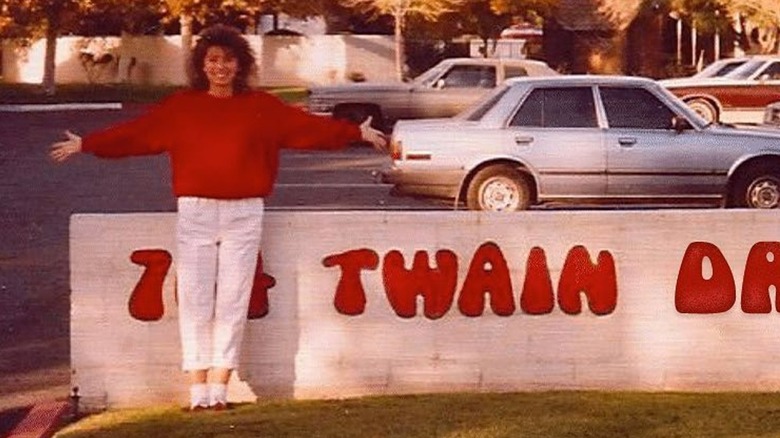 Shania Twain posing with her arms out next to a sign