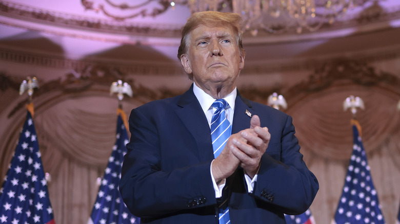 Donald Trump standing in navy suit near flags