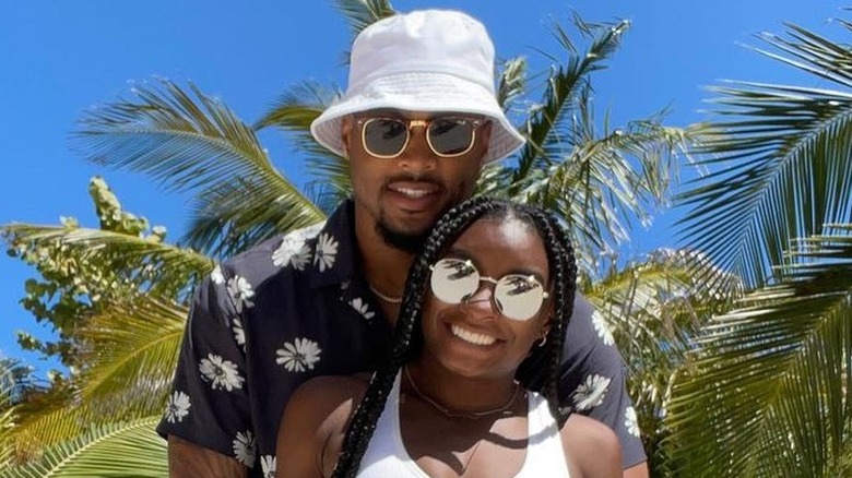 Jonathan Owens in a floral shirt and white bucket hat and Simone Biles in a white tank top